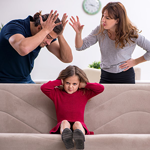 Child covering ears while parents argue; the impact of high-conflict divorce on children.